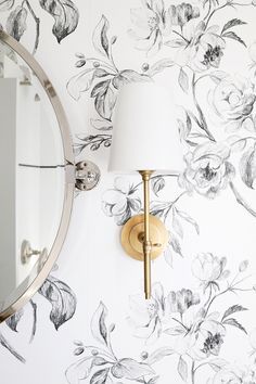 a wall with a mirror and lamp on it next to a flowered wallpaper