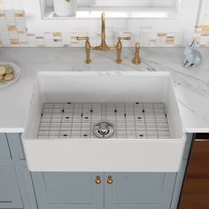 a white kitchen sink sitting under a window next to a counter with gold faucets