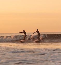 two people riding surfboards on top of a wave in the ocean at sunset or dawn