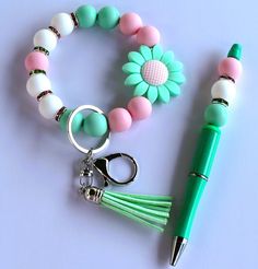 a pen, keychain, and flower charm on a white table with a green ballpoint pen