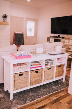 a living room filled with furniture and baskets on top of the coffee table in front of a flat screen tv