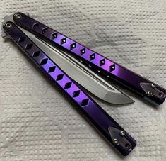 two knifes sitting on top of each other on a white sheet with purple and black accents