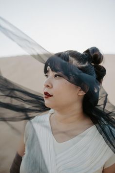 a woman with her hair blowing in the wind, wearing a white dress and black veil