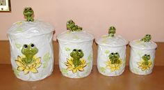 four ceramic frog canisters with lids on the floor next to a pink wall