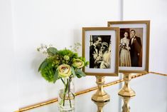 two framed pictures sit on top of a glass table next to a vase with flowers