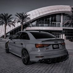 a grey car parked in front of a large building with palm trees around the perimeter