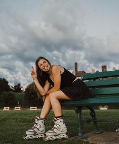 a woman sitting on top of a green bench in front of a sky filled with clouds