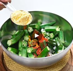 a person is stirring some vegetables in a bowl with a spoon and seasoning flakes on the side