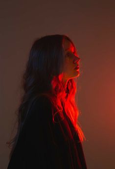 a woman with long hair standing in front of a red light and looking off into the distance