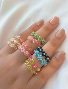 a woman's hand with five different colored rings on her fingers and one is wearing a ring made out of beads