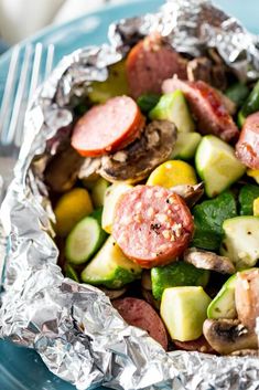 a close up of a plate of food with meat and vegetables on foil wrappers