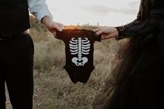 a man and woman holding up a skeleton bodysuit in the middle of a field