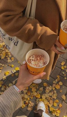 two people are holding drinks in their hands and looking at the ground with fallen leaves on it