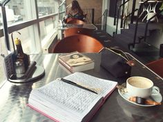 a table with a book, coffee cup and pen on it next to a window