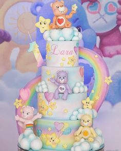 a three tiered cake with teddy bears on the top and rainbow in the background