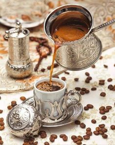 coffee being poured into a cup on top of a saucer and surrounded by coffee beans