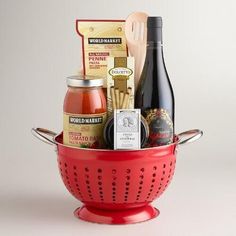 a red colander filled with wine, cheese and condiments next to a bottle of wine