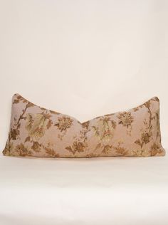 a decorative pillow on a white bed with a flowered design in gold and pink