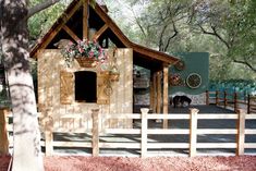 a dog house built into the side of a wooden fence with flowers hanging from it's roof