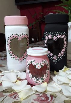 three vases with hearts painted on them sitting on a table covered in flowers and petals