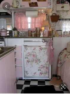 a small kitchen with pink walls and floral curtains on the window sill above the stove