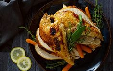 a roasted turkey with carrots and herbs on a black plate