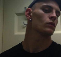 a man with ear piercings looking at the camera while wearing a black t - shirt