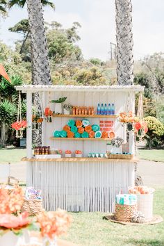 an outdoor dessert stand with orange and blue treats on it's display shelf, surrounded by palm trees