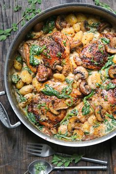 a pan filled with chicken and mushrooms on top of a wooden table next to utensils