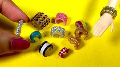 a hand holding a bunch of rings on top of a yellow table next to a doll