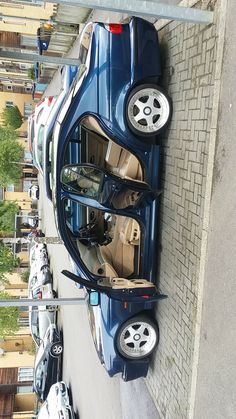 a blue car parked on the side of a road next to a building with its doors open