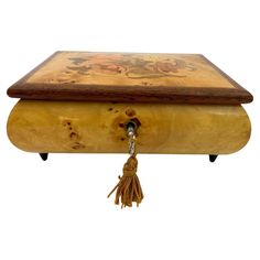 a wooden box with a tassel hanging from it's side and an ornate design on the lid