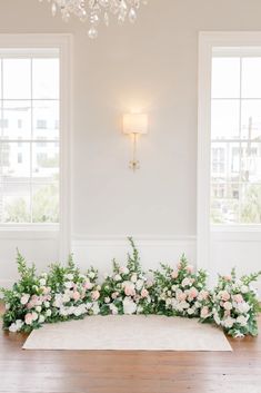 an arrangement of flowers and greenery is arranged on the floor in front of two windows