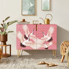 a pink cabinet with two white birds painted on the front and sides, sitting next to a potted plant