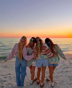 four girls standing on the beach with their arms around each other as the sun sets