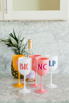 three painted wine glasses sitting on top of a counter next to a pineapple bottle