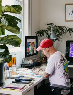 a man sitting at a desk in front of a computer monitor with tattoos on his arm