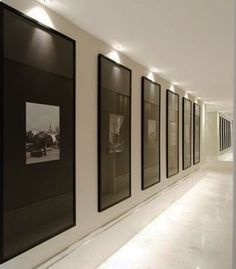 an empty hallway with black and white framed pictures on the wall, along with lights