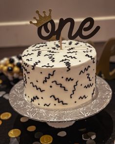 a white and black cake with a one on top is surrounded by confetti