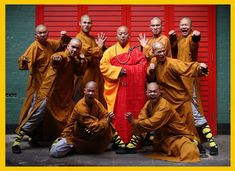 a group of monks pose for a photo in front of a red door with their hands up