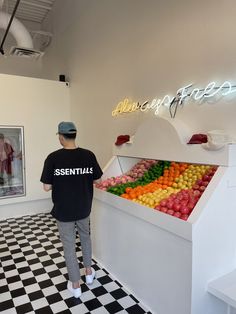 a man standing in front of a display case filled with apples and oranges on a black and white checkered floor