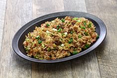 a black bowl filled with rice and meat on top of a wooden table next to a fork