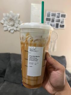 a person holding up a plastic cup filled with liquid and ice cream in front of a couch