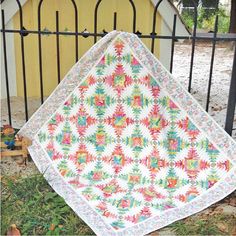 a quilt is laying on the ground next to a fence and some plants in front of it