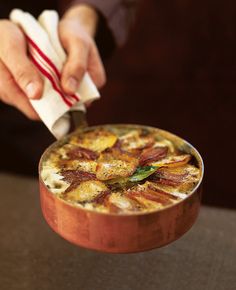 a person is holding a napkin over a food dish in a copper bowl on a table