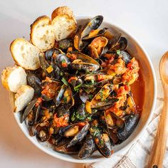 a bowl filled with mussels and bread on top of a white tablecloth