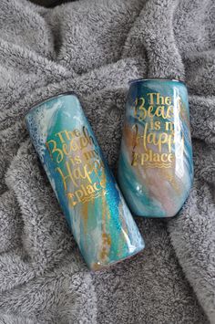 two painted wine glasses sitting on top of a gray blanket next to each other with gold lettering