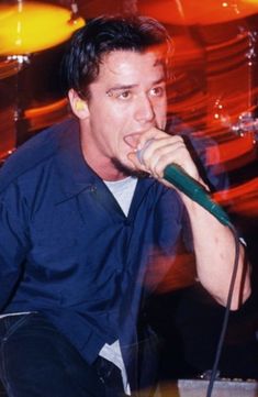 a man sitting down while holding a microphone to his mouth and singing into a mic