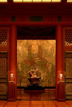 a statue is sitting in the middle of a room with red pillars and walls that have intricate carvings on them