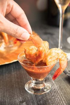 a person dipping some food into a small glass bowl on a table with wine glasses in the background